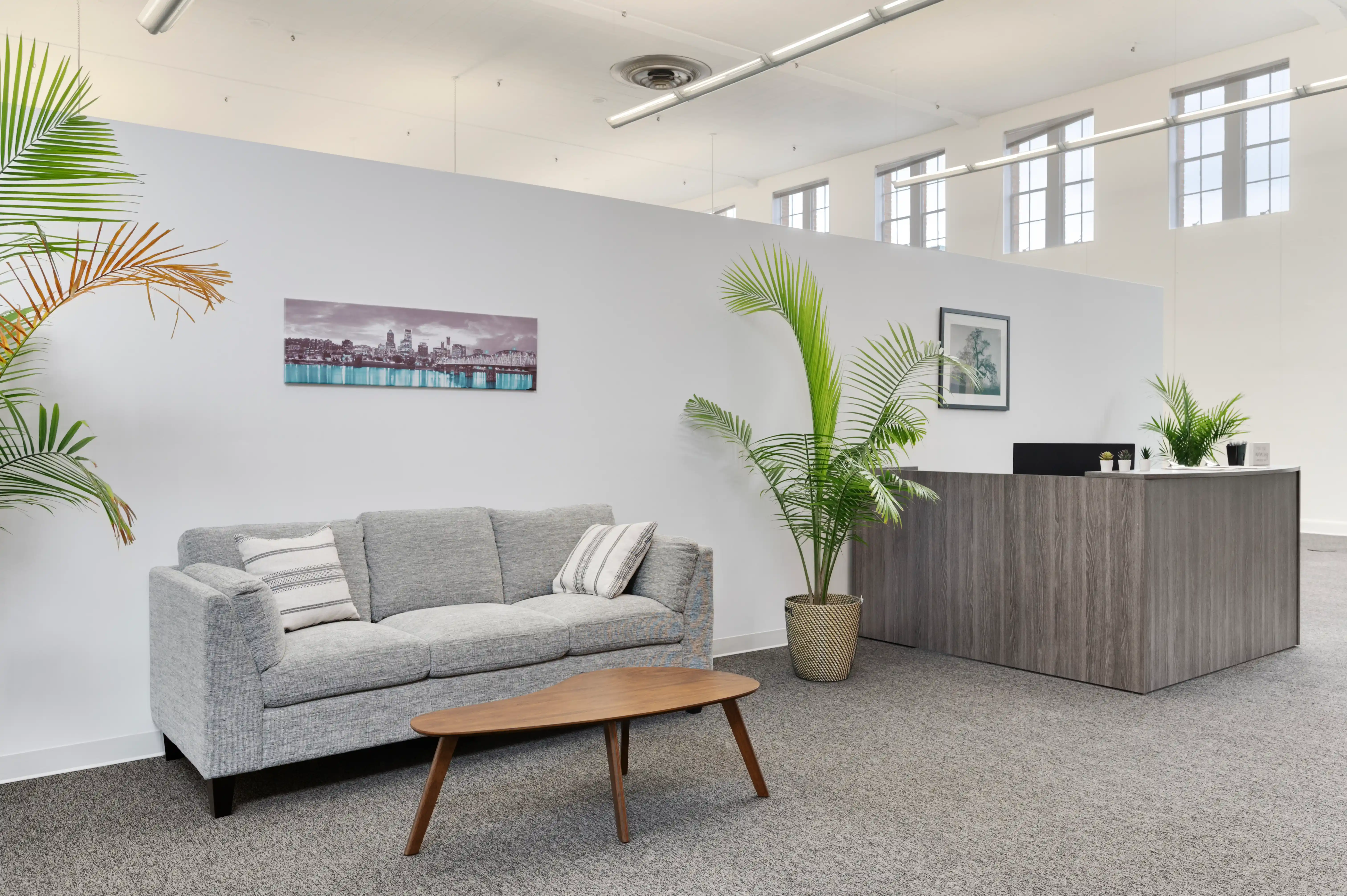 Waiting area with grey sofa, coffee table, and palm plant at Atlas Treatment Center