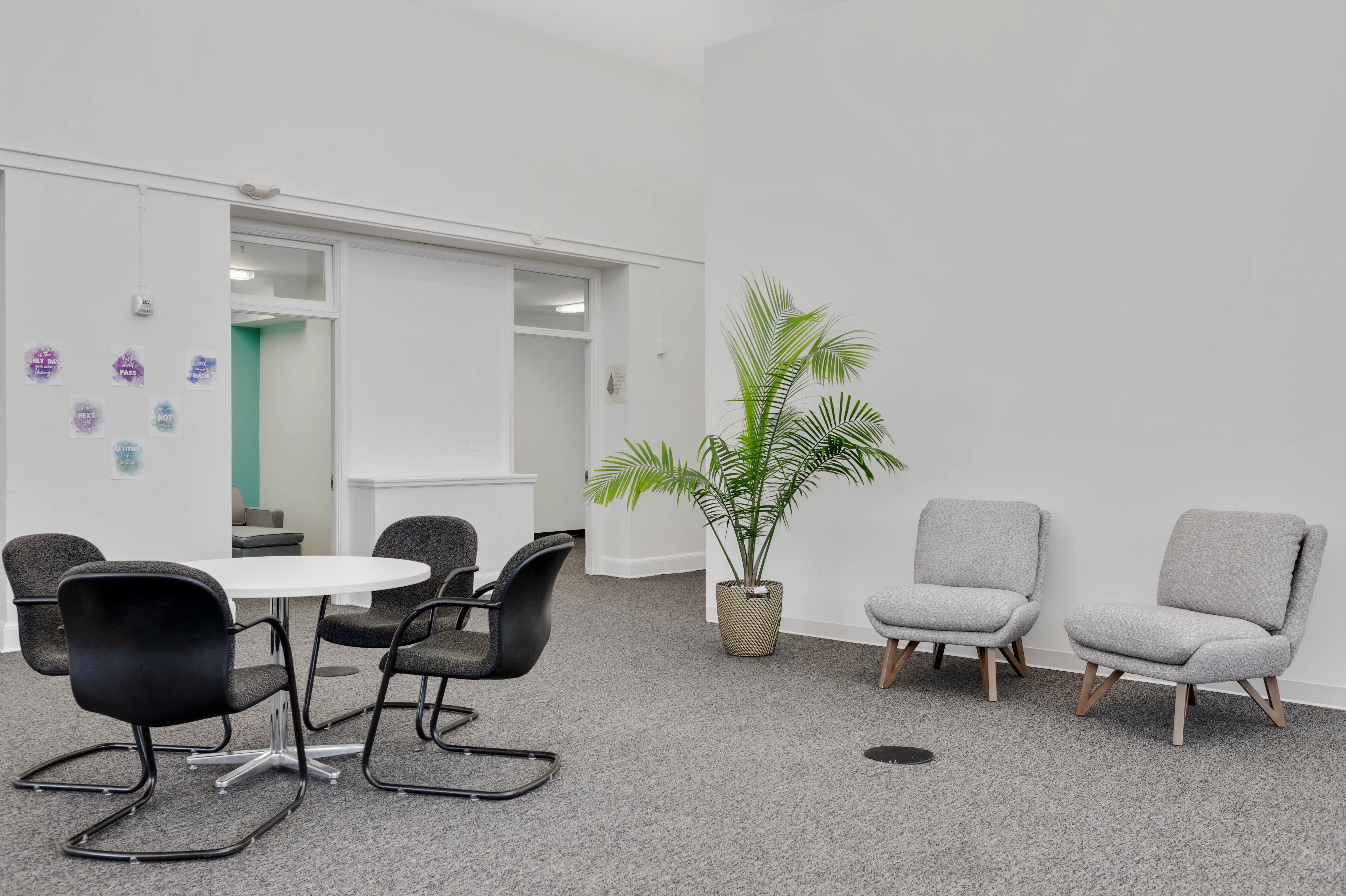 Small group seating area with round table, recovery affirmations on wall, and counseling room at Atlas Treatment Center